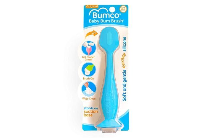 Blue silicone brush stands upright on packaging, designed for applying diaper cream. Circular icons demonstrate application steps: get diaper cream, brush on, wipe clean.