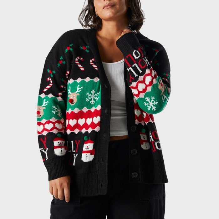 Cardigan with colorful Christmas patterns and text â€œHOLLY JOLLY,â€ worn by a person in a white top, standing against a plain background.