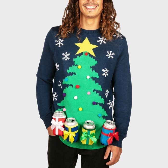 Sweater displays a decorated Christmas tree with snowflakes; four beverage can holders attached below, each wrapped with colorful ribbons. Man standing against a plain background.