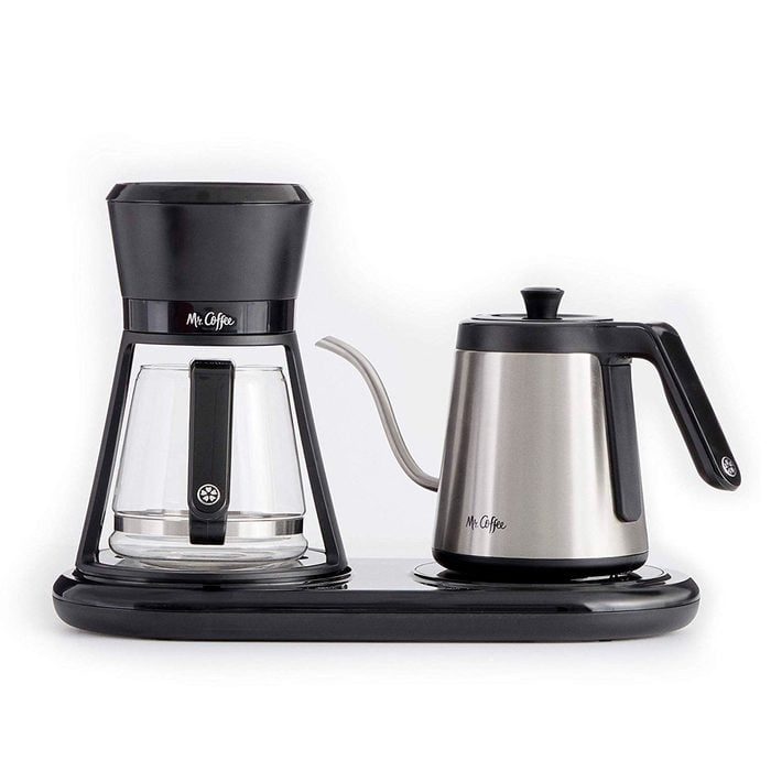 Coffee maker sits on a black base, featuring a clear glass pot and metallic gooseneck kettle labeled 