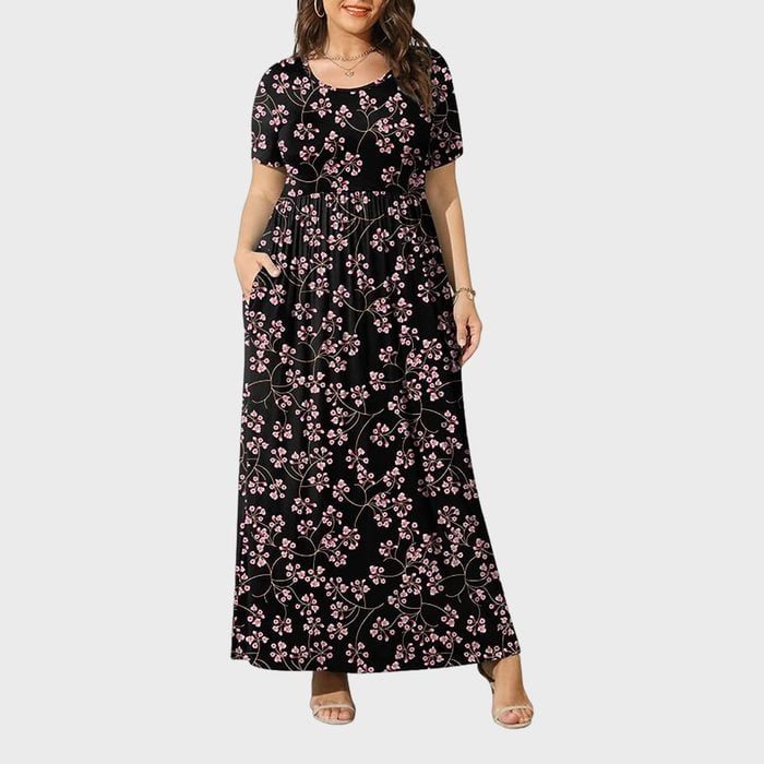 A black floral-patterned maxi dress is worn by a person standing against a plain gray background, displaying a relaxed, elegant pose.
