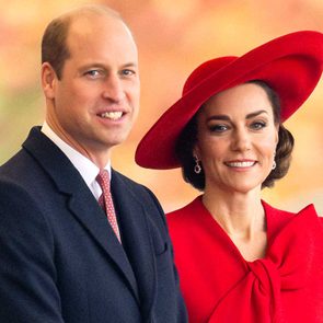 A man in a suit and a woman in a red outfit smile together against a blurred, colorful background.