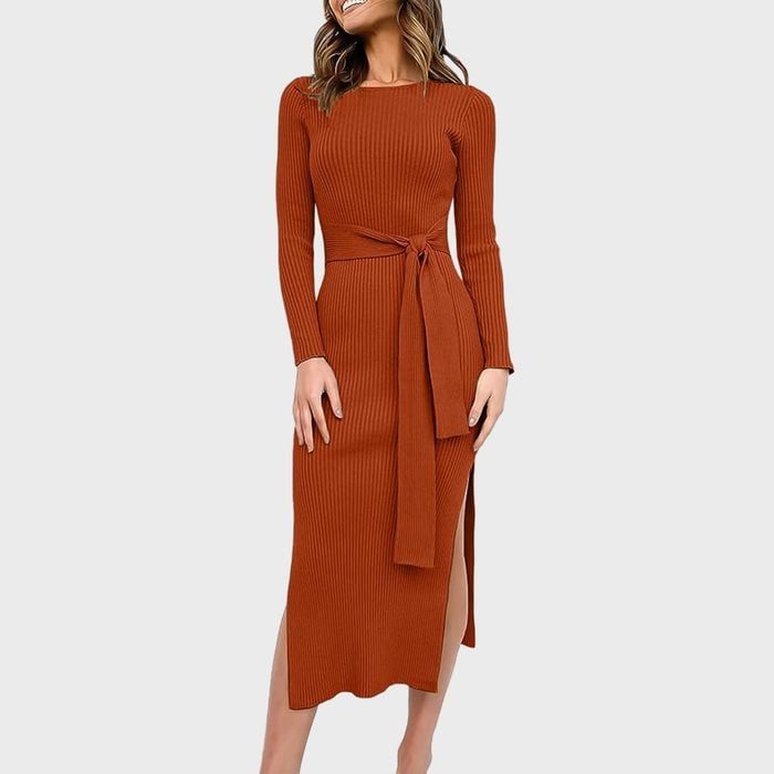 Woman wearing a long-sleeved, rust-colored ribbed dress with a waist tie, smiling in a neutral background.