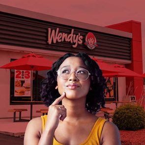 A person ponders outside a Wendy's restaurant with red umbrellas and a sign displaying 