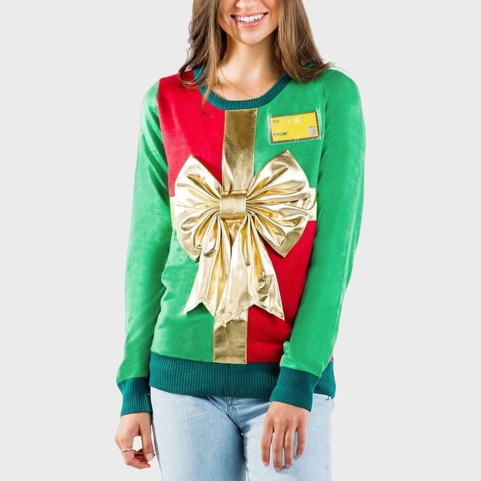 A festive sweater displays a large gold bow and gift tag design; worn by a person against a plain background.