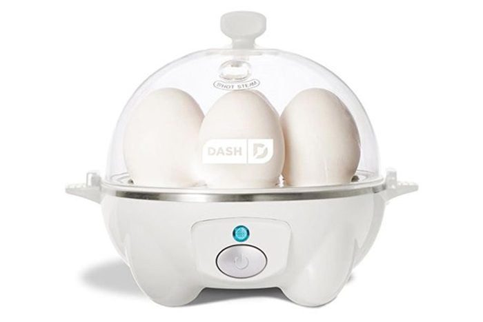 Eggs sit in a white egg cooker with a clear dome lid, in a kitchen setting.