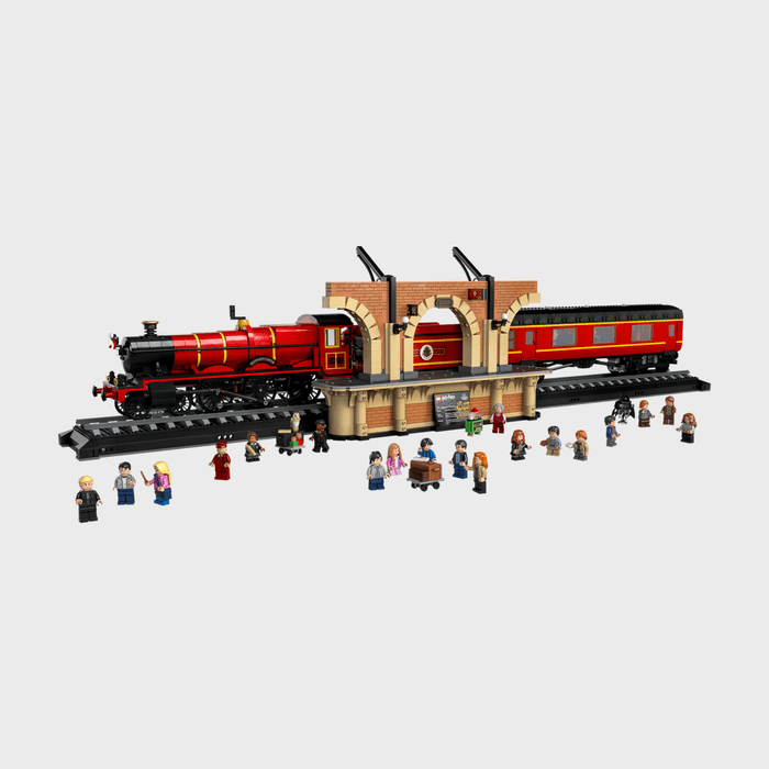 Toy train on track, surrounded by minifigures, against a brick-style station platform, creating a lively scene with diverse characters.