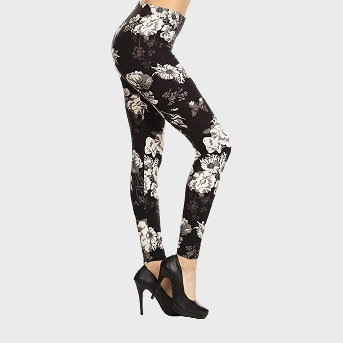 Legs wearing floral-patterned leggings stand poised in black high heels against a plain gray background.