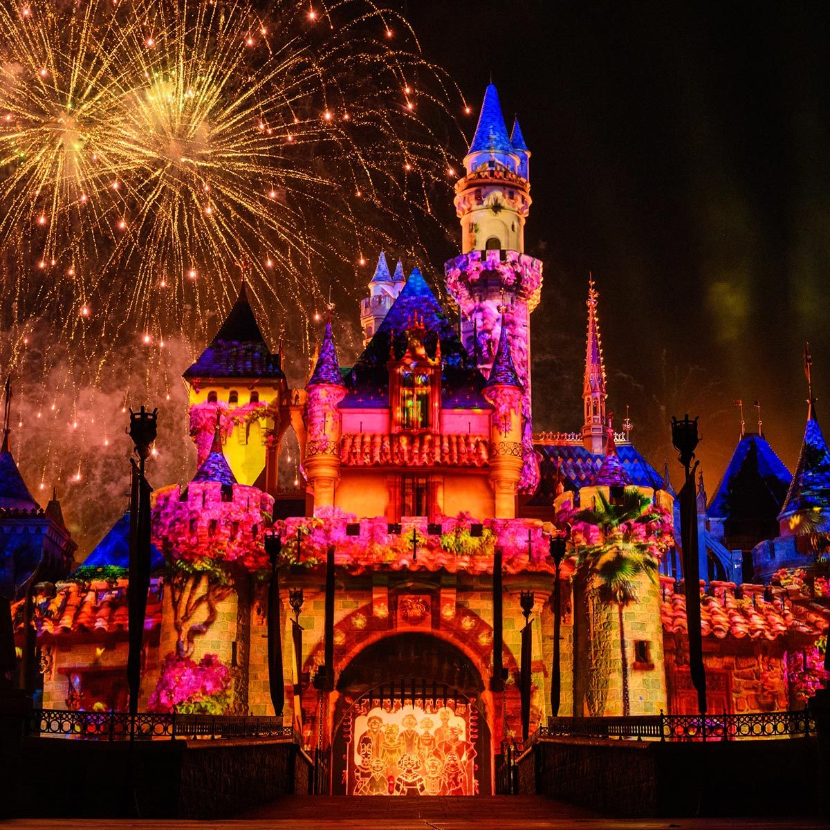 Sleeping Beauty's castle at Disneyland at night with a colorful projection and fireworks in the background