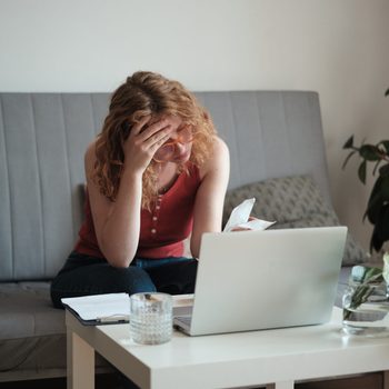 Worried woman looking at forms and receipts sitting at laptop