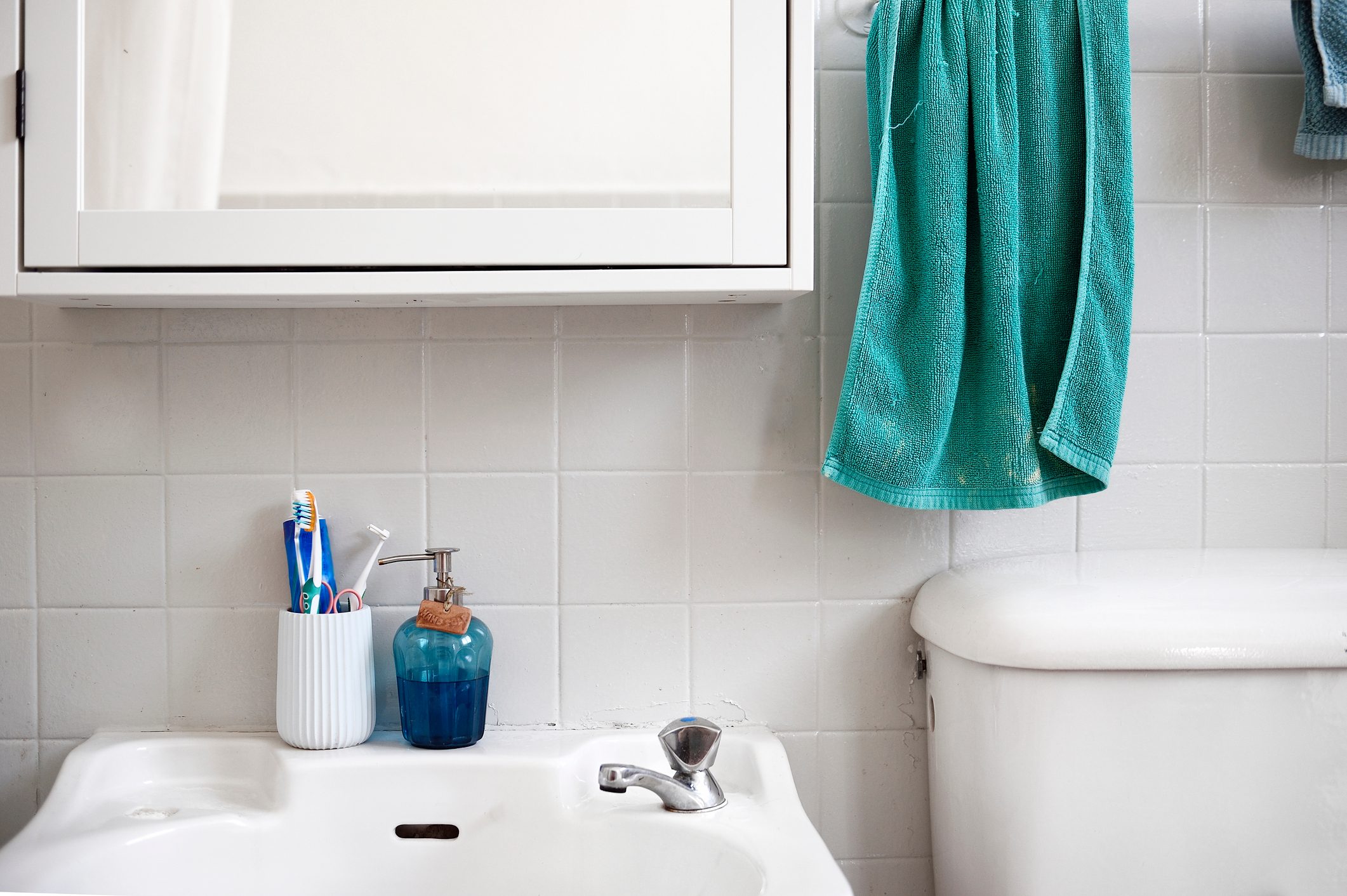 Tooth brush cup and soap dispenser on a bathroom sink next to a toilet