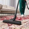 A person hoovering carpet with vacuum cleaner in room.
