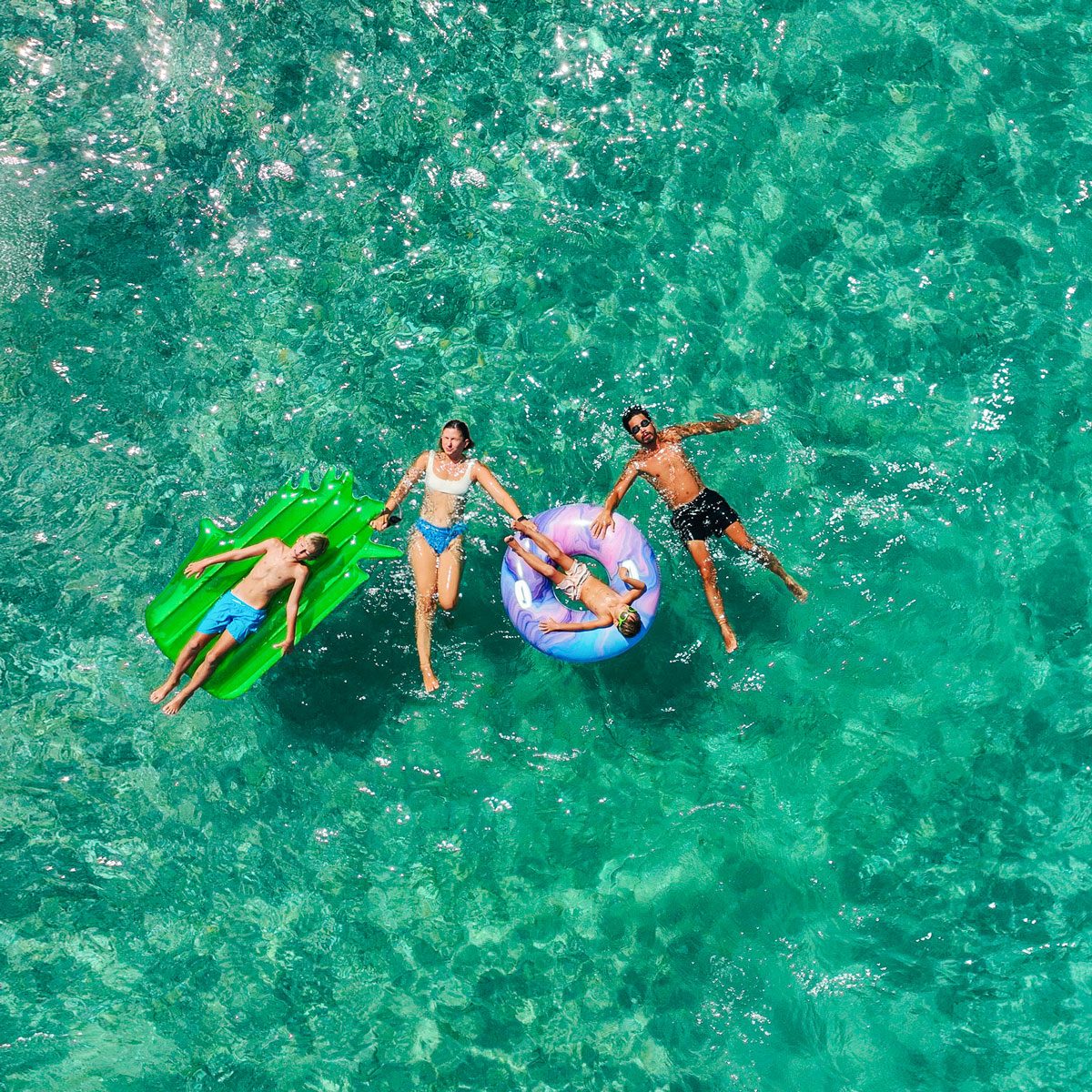 Happy Family Relaxing On The Inflatable Swim Rings In Green Ocean